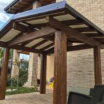 Tettoia in legno scuro per ingresso casa con travi a vista e copertura inclinata
